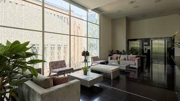 Un vestíbulo espacioso con diseño moderno, que incluye una zona de estar con sofás y sillones, una mesa de centro, y un ventanal con vistas al exterior.