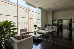 A spacious lobby with a modern design, featuring a seating area with sofas and armchairs, a coffee table, and a large window offering a view of the outside. - Bh Poblado (Medellín)
