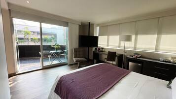 Una habitación de hotel con cama, escritorio, silla, televisor y puerta corrediza de vidrio que da a un espacio exterior.
