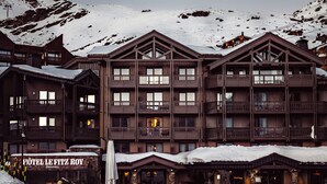 Un hôtel à plusieurs étages, doté de balcons, d’une entrée enneigée et surplombant un paysage montagneux.