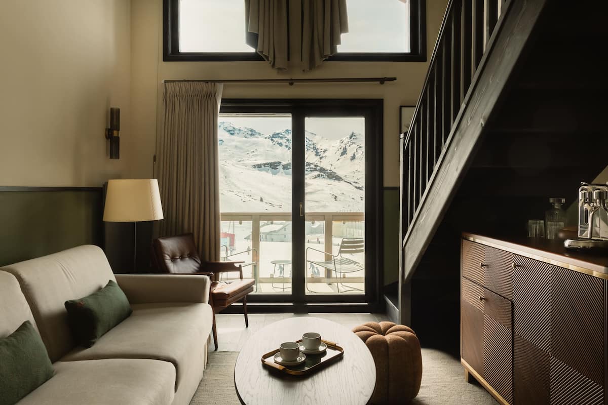 A modern living room with a sofa, a coffee table, and a view of a snowy mountain landscape through a large sliding door.