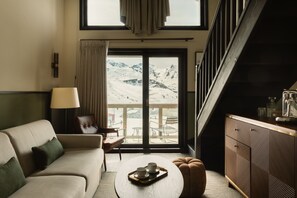 En moderne stue med sofa, sofabord og udsigt til et sneklædt bjerglandskab gennem en stor skydedør.