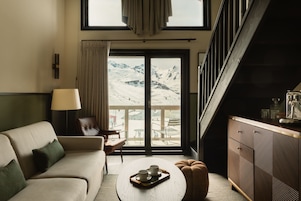 Una sala de estar moderna con un sofá, una mesa de centro y vistas a un paisaje montañoso nevado a través de un gran ventanal corredizo.