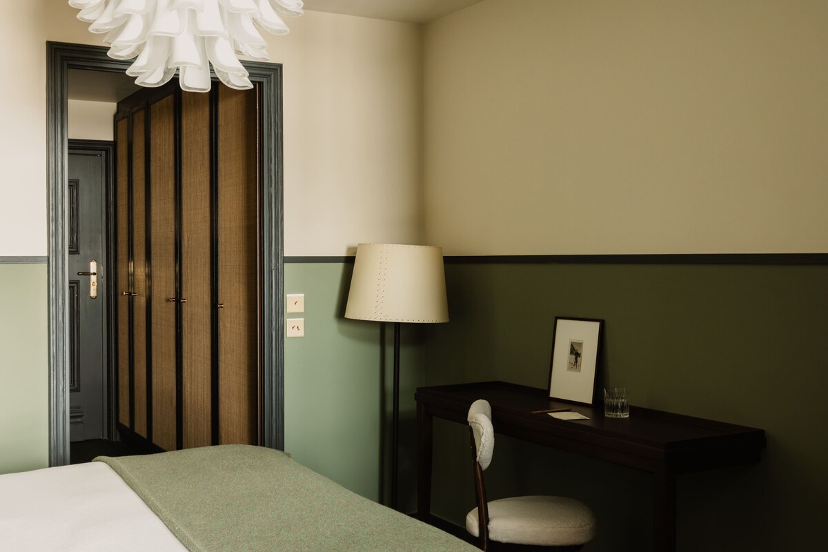 A hotel room with a bed, a desk with a chair, a lamp, and a door leading to a closet.
