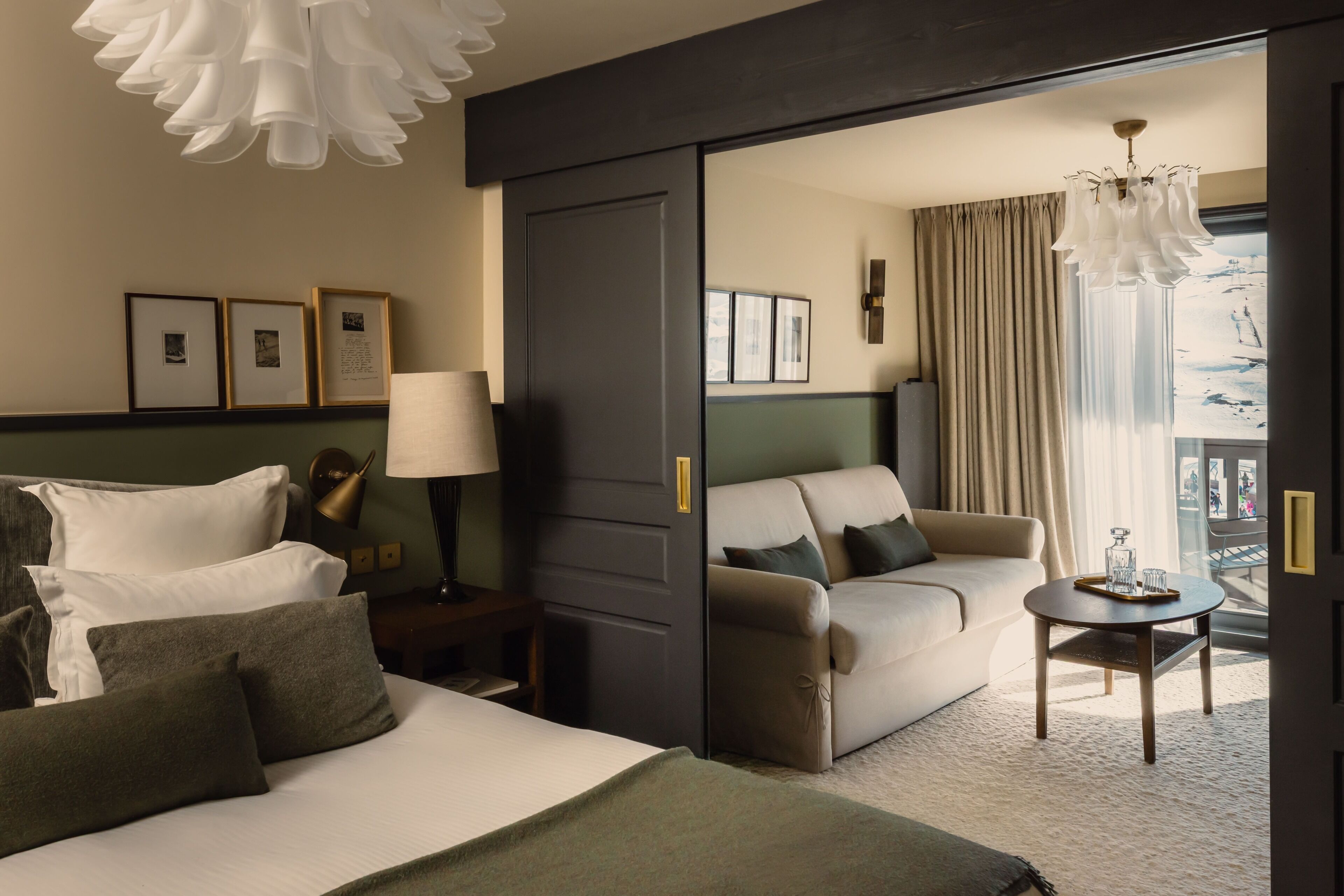 A hotel room with a bed, a sofa, a small table, a lamp, and a view of the outdoors.