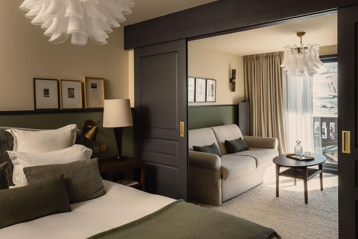 A hotel room with a bed, a sofa, a small table, a lamp, and a view of the outdoors.