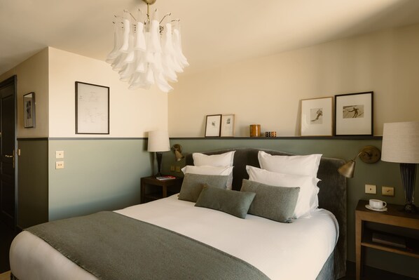A neatly made bed with pillows, a bedside table with a lamp, and framed pictures on the wall. - Le Fitz Roy (Les Belleville)