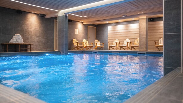 Une piscine intérieure avec des chaises en bois et une pile de serviettes.