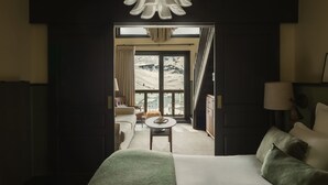 Et hotelværelse med en stor seng, et lille bord, en sofa og udsigt til et bjerglandskab gennem et stort vindue.