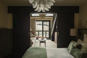 Habitación de hotel con una cama grande, una mesita pequeña, un sofá y vistas a un paisaje montañoso a través de un ventanal.