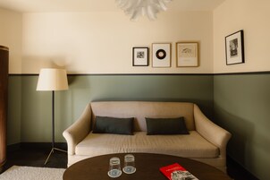 A room with a sofa, a coffee table with glasses and a book, and framed pictures on the wall.