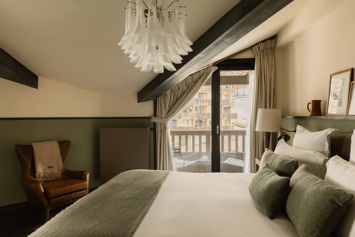 A hotel room with a large bed, a chair, a lamp, and a view of the outside balcony.