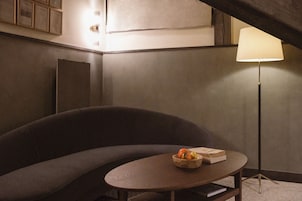 Una habitación con sofá, una mesa con un frutero y libros, una lámpara de pie y un aplique de pared.