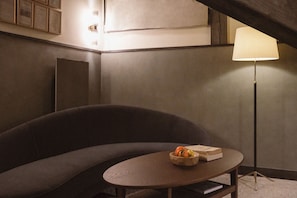 A room with a sofa, a table with a bowl of fruit and books, a floor lamp, and a wall-mounted light fixture. - Le Fitz Roy (Les Belleville)