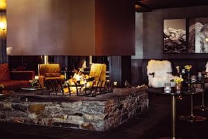 A stone fireplace with chairs around it, a fur-covered chair, and a table with candles.