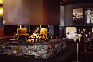 A stone fireplace with chairs around it, a fur-covered chair, and a table with candles. - Le Fitz Roy (Les Belleville)