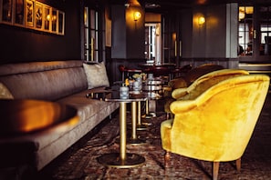 A dimly lit lounge area with a sofa and armchairs, a patterned carpet, and wall-mounted light fixtures. - Le Fitz Roy (Les Belleville)