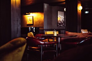 A dimly lit bar area with leather seating, a table with a mug, and framed artwork on the walls. - Le Fitz Roy (Les Belleville)