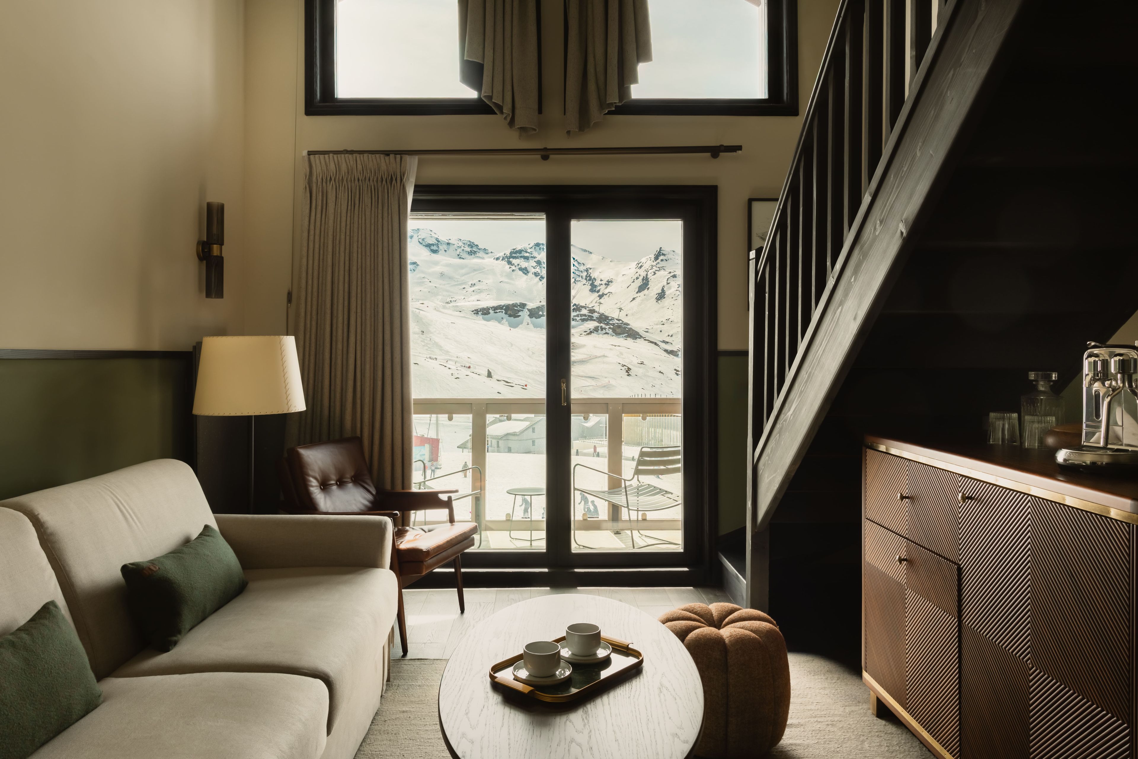 Un salon moderne avec un canapé, une table basse et une vue sur un paysage montagneux enneigé, visible à travers une grande porte coulissante.