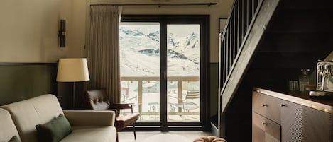 Un salon moderne avec un canapé, une table basse et une vue sur un paysage montagneux enneigé, visible à travers une grande porte coulissante.