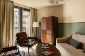 A hotel room with a sofa, a chair, a lamp, a cabinet, and a table with glasses and a book. - Le Fitz Roy (Les Belleville)