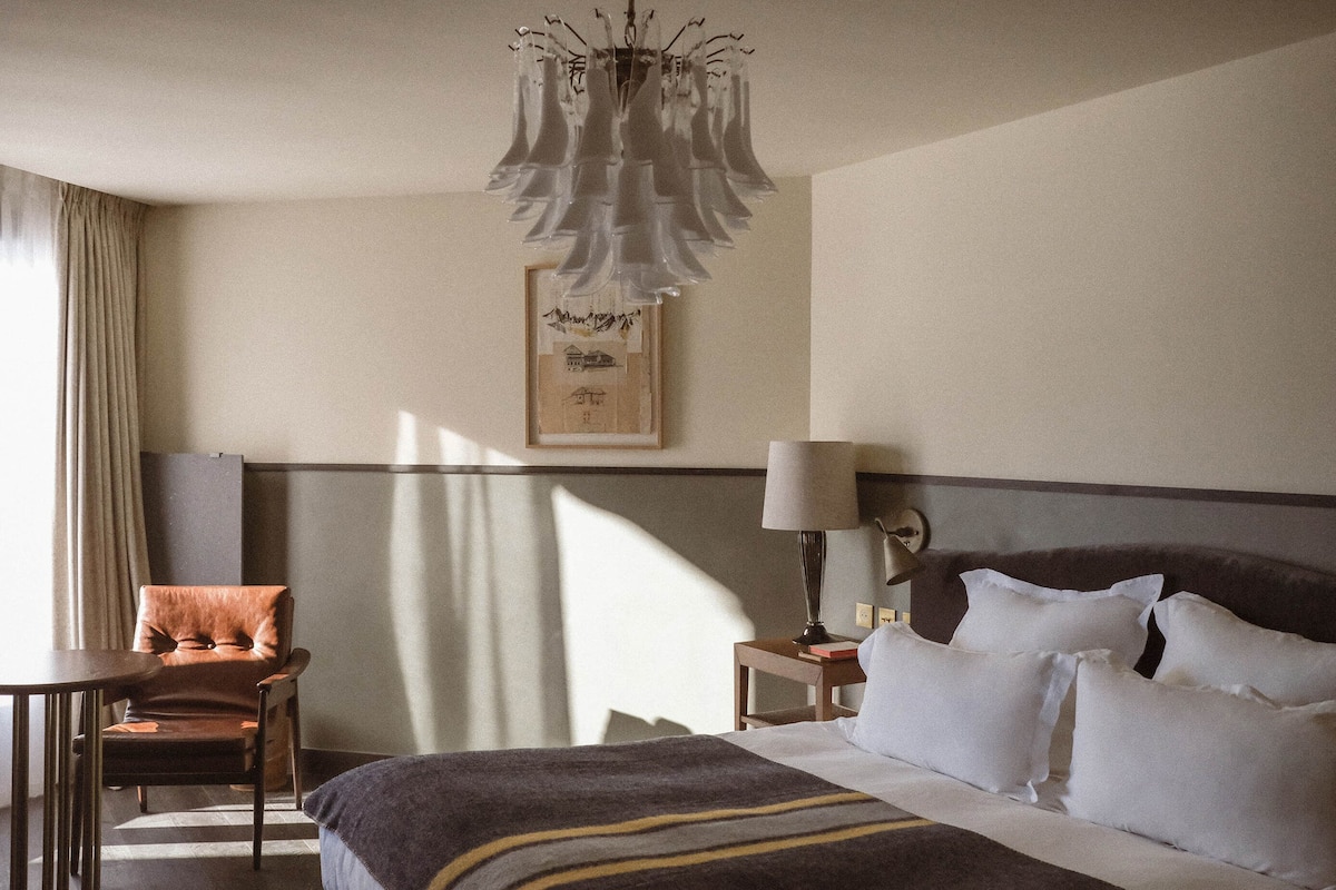 A hotel room with a bed, a desk, a chair, a lamp, and a framed picture on the wall.