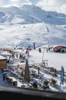 Ein verschneiter Außenbereich mit Tischen und Stühlen, einer Holzkonstruktion und einem Blick auf die Berge.