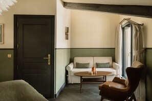 A room with a dark door, a white sofa with green cushions, a round wooden table, and a leather armchair. - Le Fitz Roy (Les Belleville)