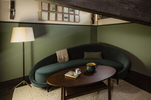 Ein gemütliches Zimmer mit einem grünen Sofa, einem runden Couchtisch, einer Lampe und gerahmten Zertifikaten an der Wand.