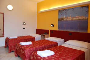 Une chambre d’hôtel avec deux lits simples, chacun recouvert d’une couverture rouge et doté d’oreillers blancs, une table de chevet avec un téléphone et un luminaire fixé au mur.