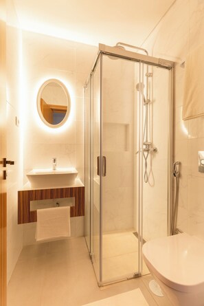 Een moderne badkamer met een douchecabine van glas, een witte wastafel met houten kastje en een ronde spiegel.