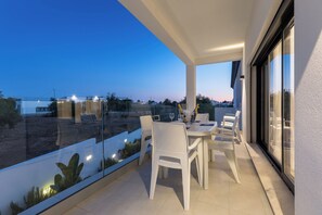 Een balkon met een tafel en stoelen, uitkijkend op een landschap met verre gebouwen en een heldere lucht.