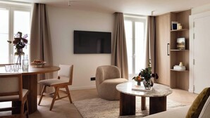 Een moderne woonkamer met een ronde salontafel, een bank, een eethoek met stoelen, een aan de muur bevestigde televisie en een boekenkast.