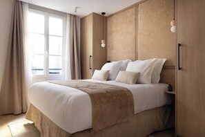 A large bed with a beige headboard and a brown throw blanket, a window with curtains, and a pendant light on the wall. - Superb Air-conditioned Apartment - Le Marais (Paris)
