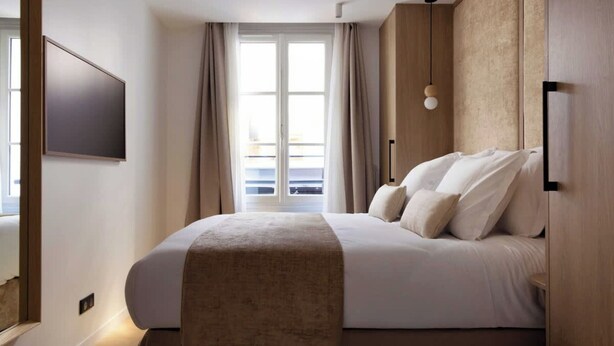Een moderne hotelkamer met een groot bed, een flatscreen televisie aan de muur en een balkon met gordijnen.