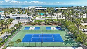 A tennis court with a pool, surrounded by palm trees and buildings. - Gulf-Front Grandeur: Your Private 2BR Beachfront Sanctuary at Villa 2628 (Captiva)