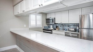A modern kitchen with white cabinetry, a stainless steel refrigerator, a microwave, and a built-in oven. - Gulf-Front Grandeur: Your Private 2BR Beachfront Sanctuary at Villa 2628 (Captiva)