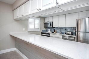 A modern kitchen with white cabinetry, a stainless steel refrigerator, a microwave, and a built-in oven. - Gulf-Front Grandeur: Your Private 2BR Beachfront Sanctuary at Villa 2628 (Captiva)