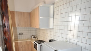 Una cocina pequeña con un refrigerador blanco, una estufa y un microondas. Hay un mueble de madera sobre la estufa y un salpicadero de azulejos.