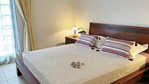 Una cama bien hecha con una cubierta acolchada, dos almohadas y una mesita de noche con una lámpara y una planta pequeña.
