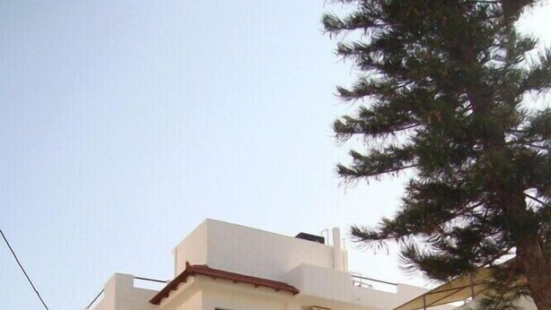 Un edificio residencial de varios pisos con balcones, entrada protegida por un portón y zonas verdes circundantes.