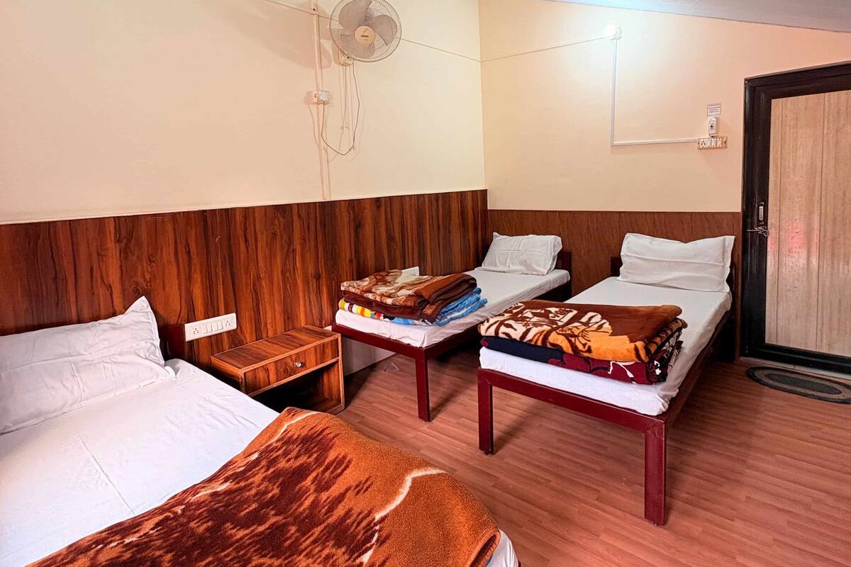 Habitación de hotel con dos camas, cabecera de madera, mesita de noche con lámpara y ventilador de techo.