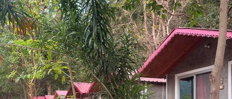 A row of cabins with red roofs, surrounded by lush greenery and a small stream.