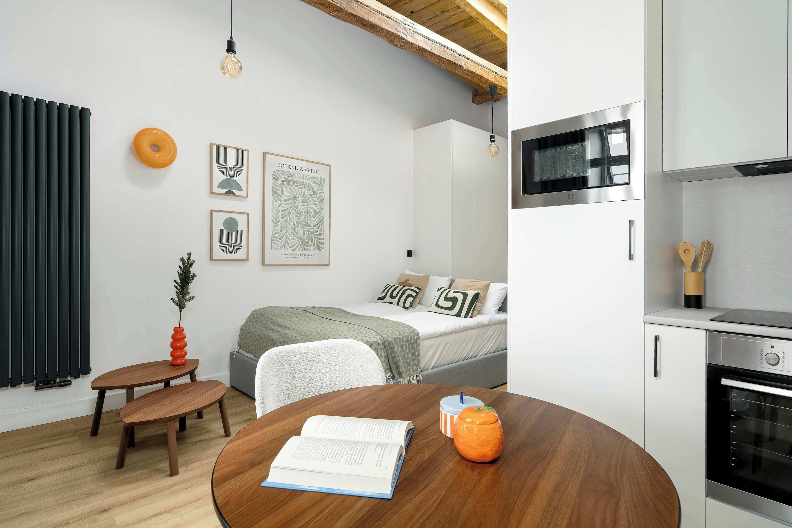 A modern, compact living space with a bed, a dining table, a kitchen area with a microwave and oven, and a small seating area.