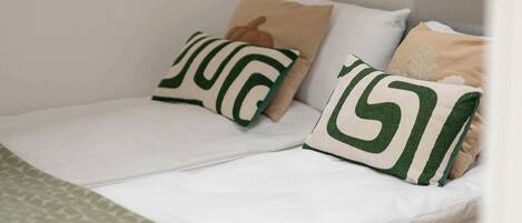 Cama con ropa blanca y dos almohadas con diseños verdes y beige.