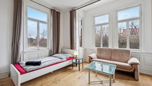 A bedroom with a single bed, a sofa, a small table, and large windows. - Fully equipped apartments in Metzingen - ideal for fitters & companies (3 units) (Metzingen)