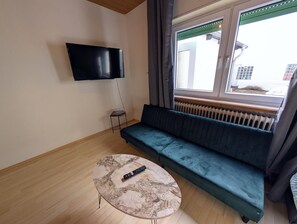 A living room with a sofa, a TV mounted on the wall, a small table, and a window with curtains. - Apartment 'Wat Bickenbach' with Wi-Fi (Bickenbach)