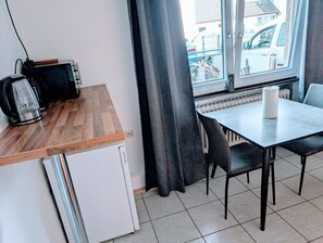 A compact kitchenette with a toaster, kettle, and refrigerator, a dining table with chairs, and a view of the street through a window. - Apartment 'Wat Bickenbach' with Wi-Fi (Bickenbach)