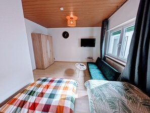 A room with a wooden ceiling, a television, a sofa, a bed with a checkered blanket, and a window with curtains. - Apartment 'Wat Bickenbach' with Wi-Fi (Bickenbach)