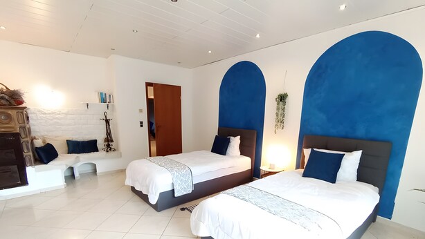 A hotel room with two beds, a sofa, a wooden cabinet, and a white tiled floor.